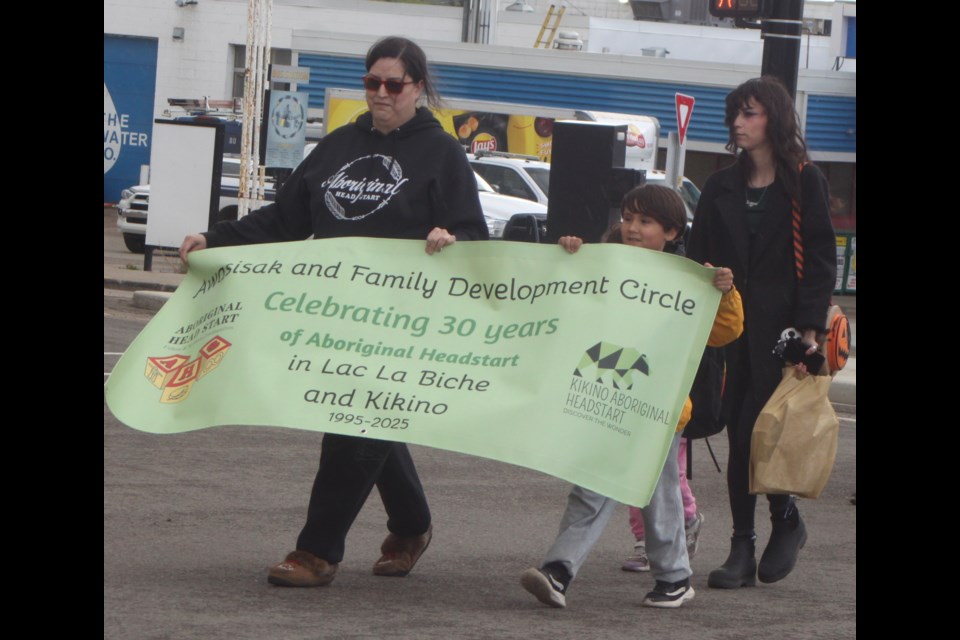 Vanessa Roesler, coordinator of the Kikino Aboriginal Head Start program, Riley Gladue, and Houston Donofrio, carry a banner marking three decades since the program was established in Lac La Biche and Kikino Métis Settlement. Chris McGarry photo. 
