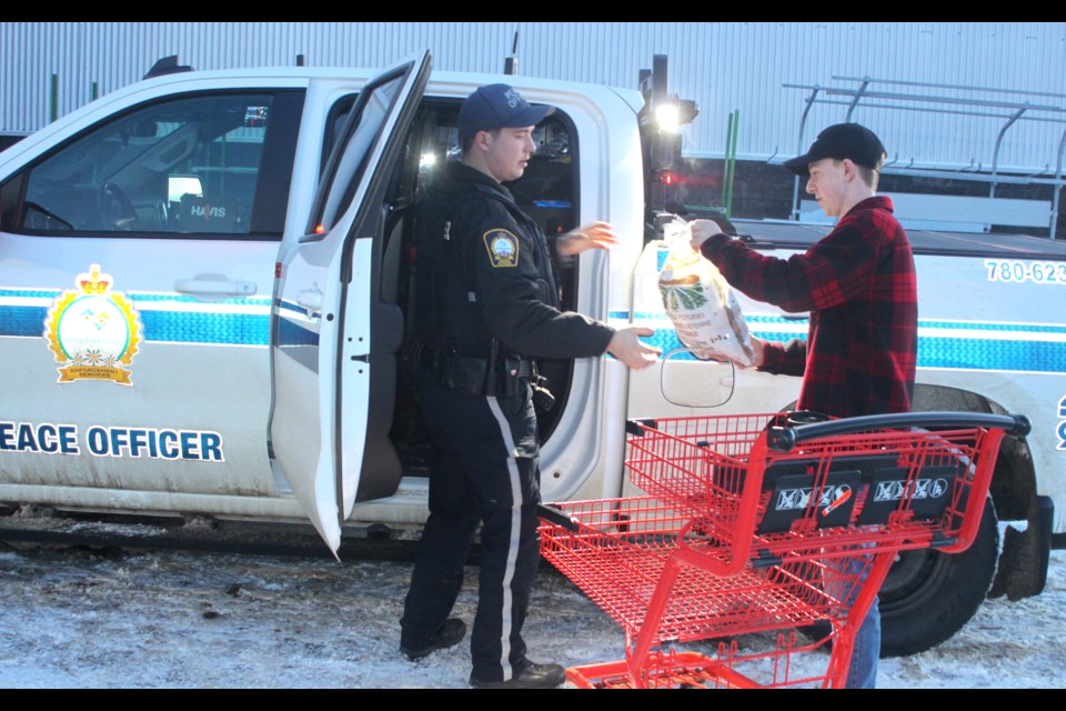 Austin Zedel, a community peace officer with Lac La Biche County Enforcement Services, gives JAWS student Braeden Cloutier a hand to load donated food items into the back of a cruiser. Chris McGarry photo. 