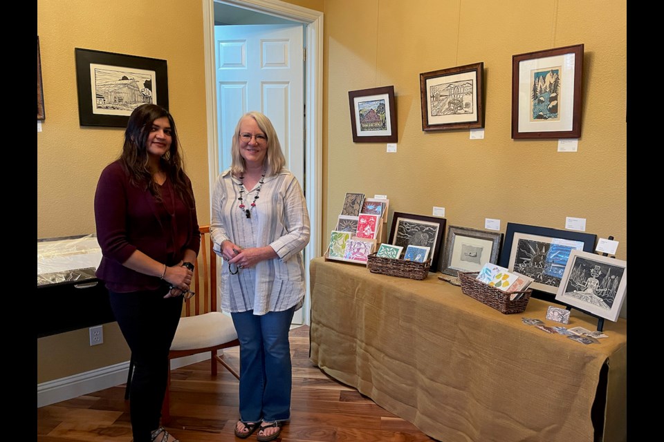 Artists Shweta Agrawal and Karen Barry stand along pieces of their work. Barry is known for her print etchings while Agrawal is a traditional acrylic and oil painter.