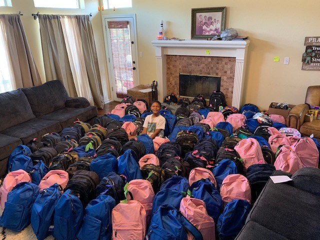 jaxson surrounded by backpacks he has donated