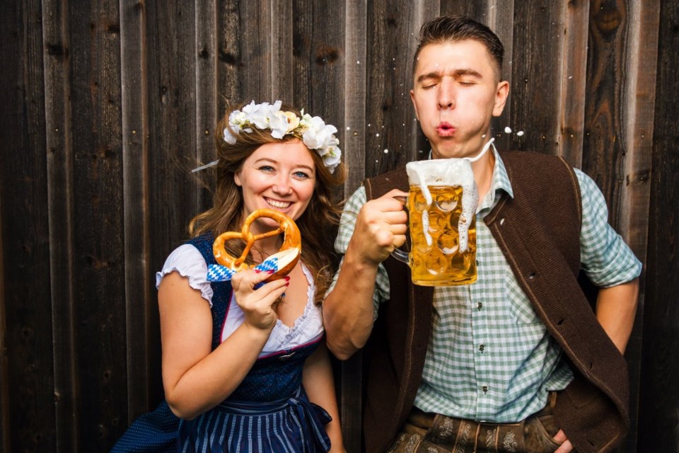 A woman holds a pretzel while a man holds a mug of beer. 