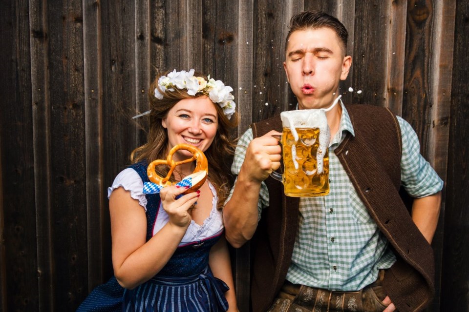 A woman holds a pretzel while a man holds a mug of beer.