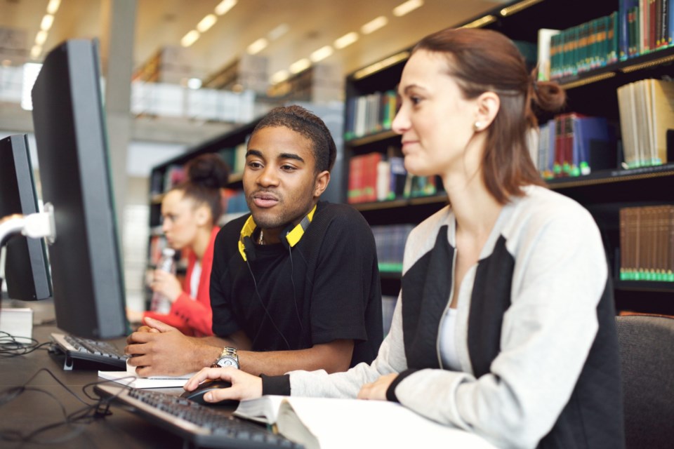 Young,University,Students,Sitting,At,Table,Using,Computers,For,Research.