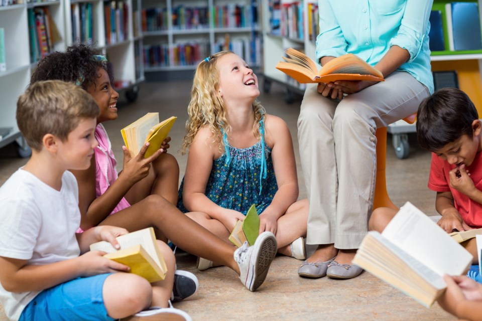 Low,Section,Of,Female,Teacher,With,Smiling,Children,Reading,Books