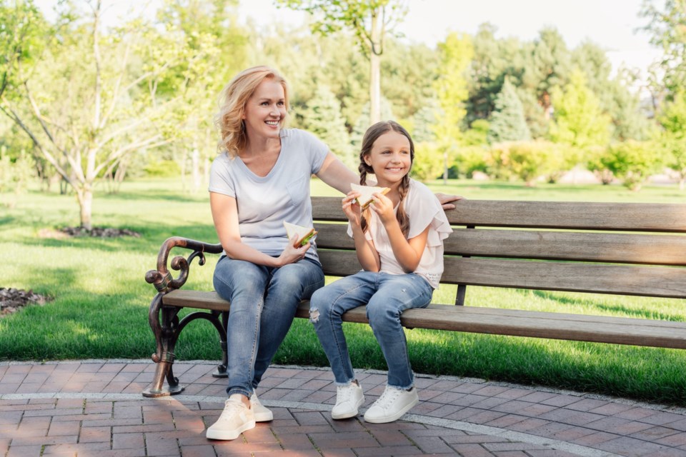 Smiling,Woman,And,Granddaughter,Eating,Sandwiches,Together,While,Sitting,On