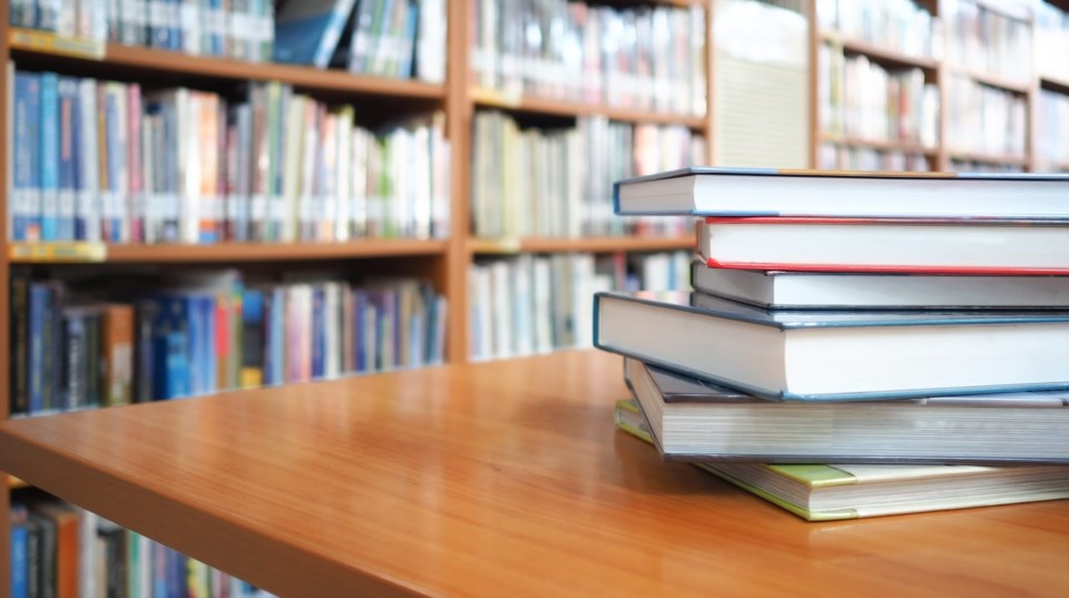 Book,Stack,On,Wood,Desk,And,Blurred,Bookshelf,In,The