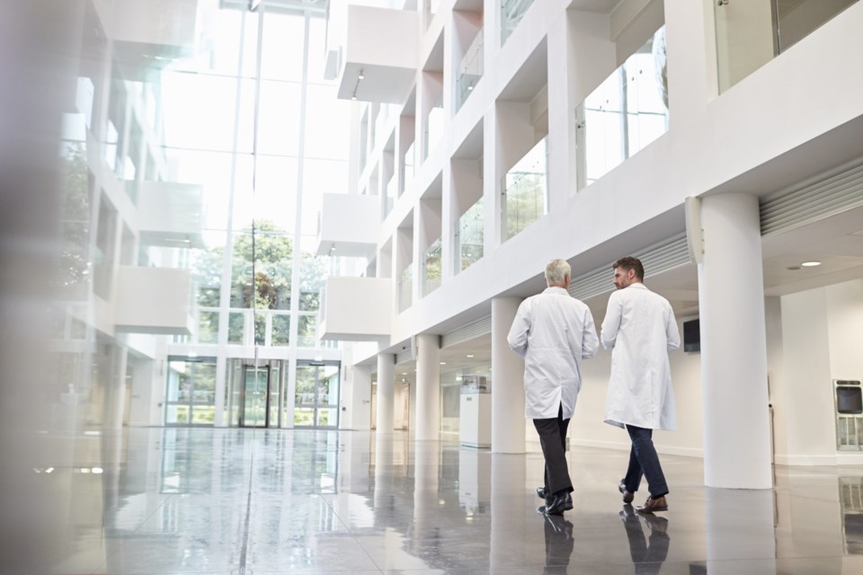 Rear,View,Of,Doctors,Talking,As,They,Walk,Through,Hospital