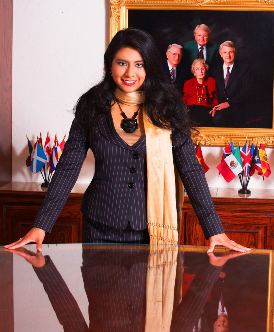 Mary Ann in suit at office with flags and family portrait (1)