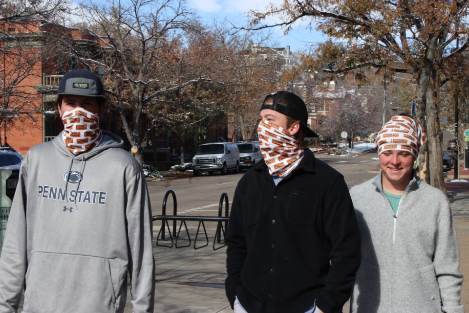 College students Colin Berg (left), Connor Dreher and Brady Bowman stroll through downtown Boulder, Colorado, in mid-November wearing matching neck gaiters. Some research suggests the thin material used in gaiters does not block as much of the coronavirus as cloth face masks do, even when worn correctly, doubled over and covering the nose and mouth. (Markian Hawryluk/KHN)