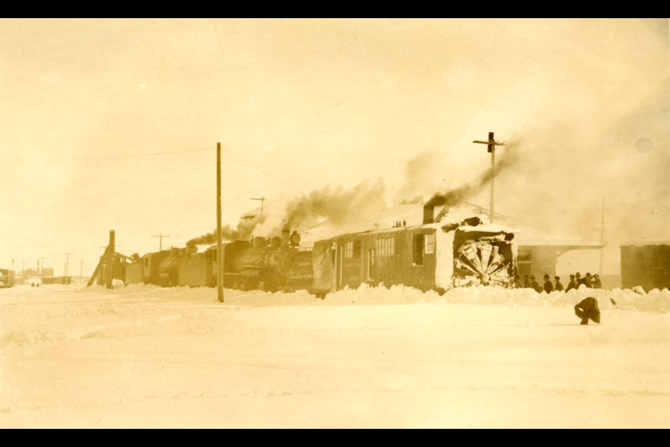 A postcard depicting a train-mounted plow clearing snow off the railroad tracks at 1st & Main in 1913