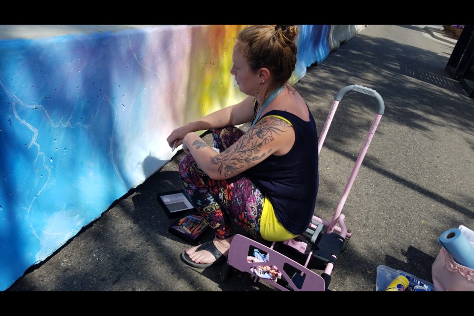 Joyanna Rose Gittings, owner of Obra Arts Studio, paints a section of the barricades along Main Street to make the area look less industrial and to attract more people downtown. 
(Photo by Monte Whaley)