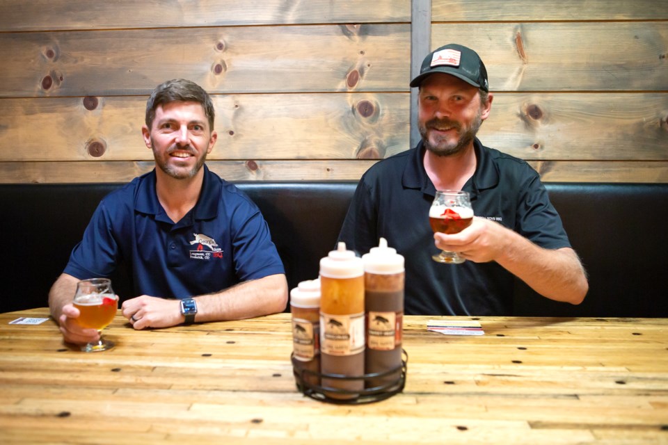 Georgia Boys BBQ founders  Matt Alexander and Nickolas Reckinger enjoy a beer at the Longmont location âThe Shackâ on July 14. Infront of them is the Georgia Boys BBQ sauces, one of the many original recipes served at the BBQ joint. Photo by Ali Mai | ali.mai.journo@gmail.com