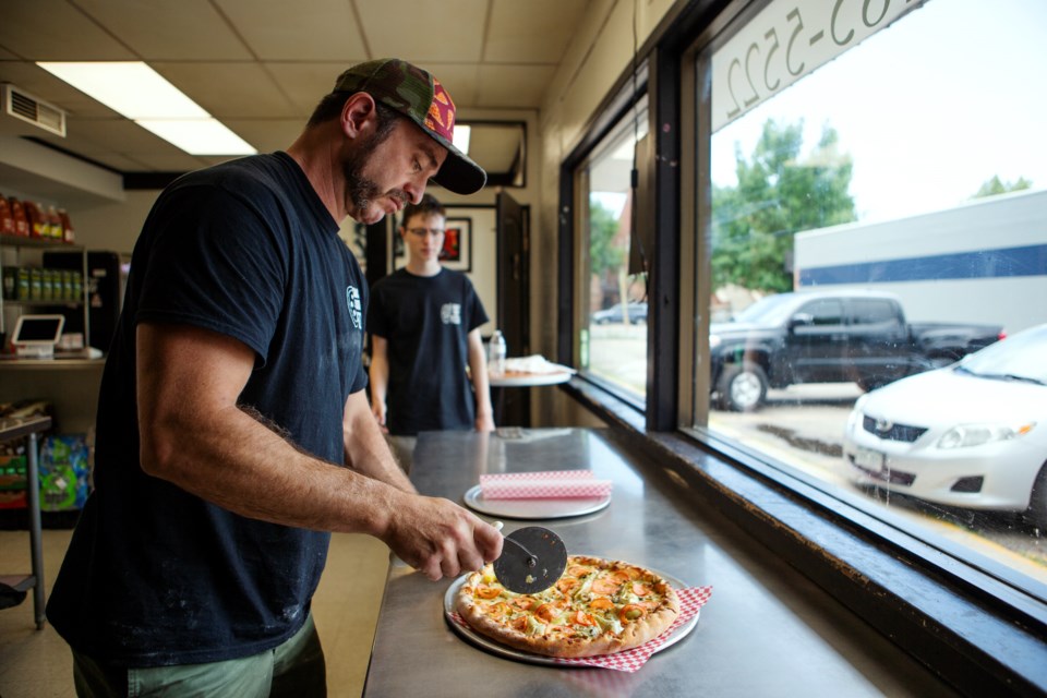 Joshua Shurtleff , owner of SmackDaddy Pizza in Longmont, cuts a âGreen Goddessâ pizza on July 5 as his son Solomon, 16-years-old, watches. Photo by Ali Mai | ali.mai.journo@gmail.com