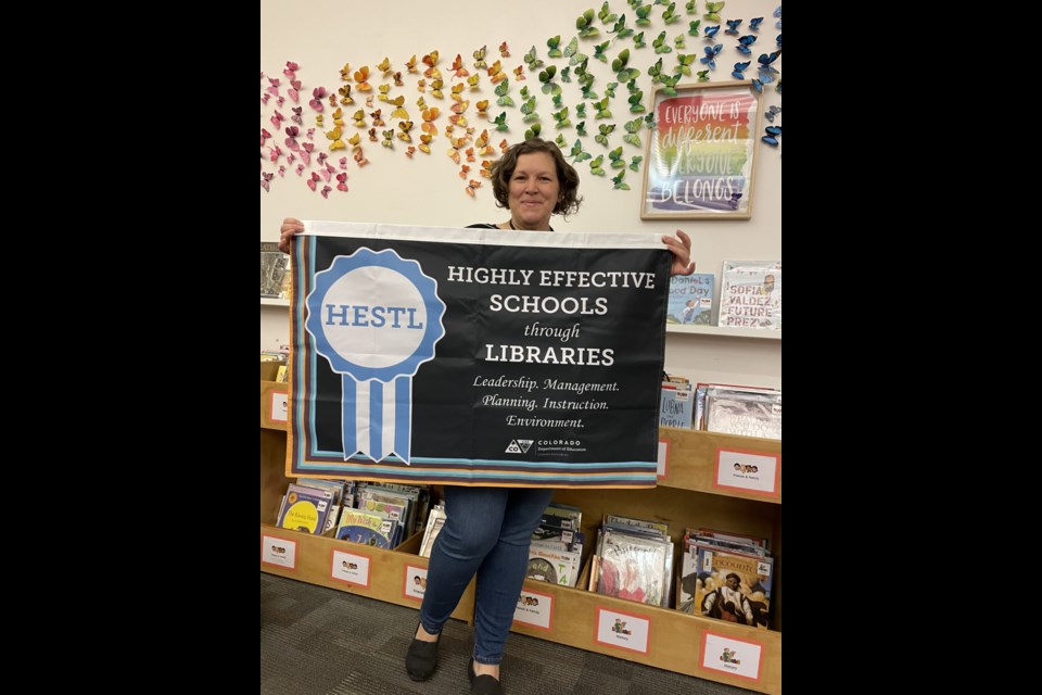 Denise von Minden holds up HESTL banner at Flagstaff Academy library