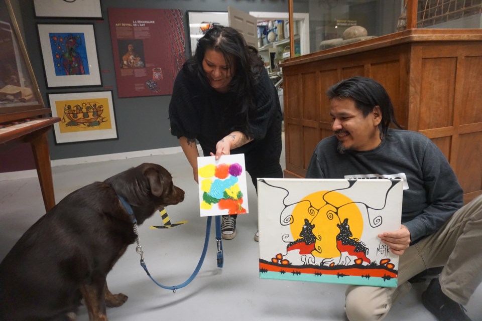 Huronia Museum executive director Nahanni Born shows Jasper his completed painting while artist Paul Whittam looks on holding one of his own paintings.
