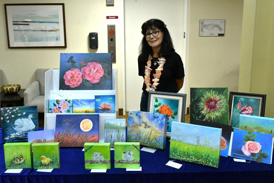 Local artist Charlene Douglas stands with a display of her oil paintings at the Atria Mulberry Estates grand reopening event recently.