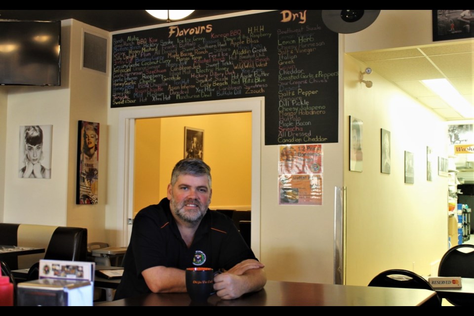 Brandon Richardson in front of a chicken wings and tenders flavour board. Staff photo