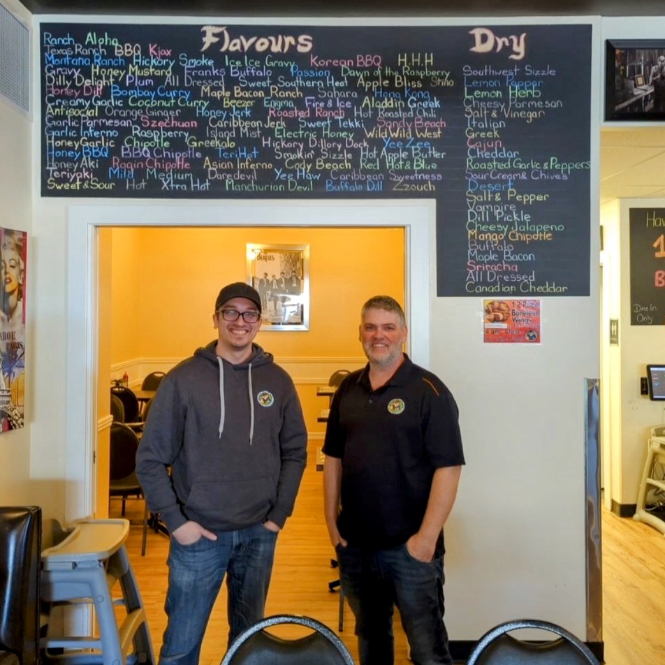 john-adams-and-brandon-richardson-in-front-of-the-famous-chicken-flavours-board