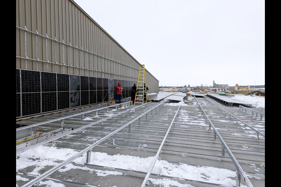 Tradesmen atop the Yara Centre roof Friday morning were well bundled against the cold. The brackets for the new solar panels have been installed, and panels are now being mounted. The Yara Centre will have 227 solar panels supplementing its energy usage