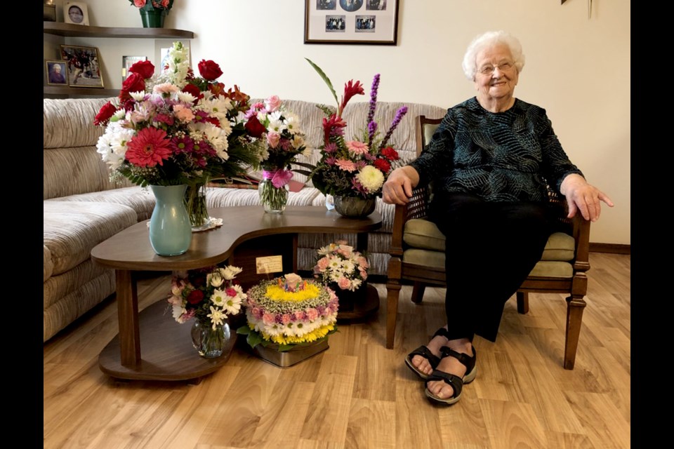 Shirley Bowler poses for a photo in her home with some of the flowers sent over by friends and family in honour of her 100th birthday.