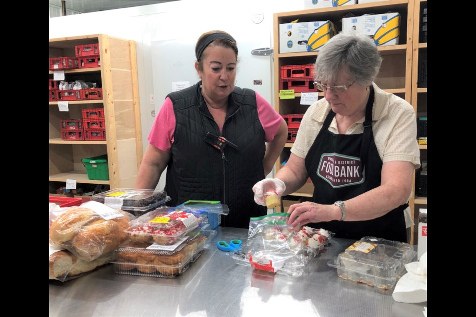 Deann Little, volunteer program co-ordinator, chats with Jeanette Stewart as she packs muffins for food hampers. Stewart has volunteered at the food bank for 24 years. Photo by Jason G. Antonio 