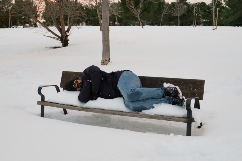 Homeless man sleeps on a snow-covered bench (Ladanifer- iStock- Getty Images Plus)