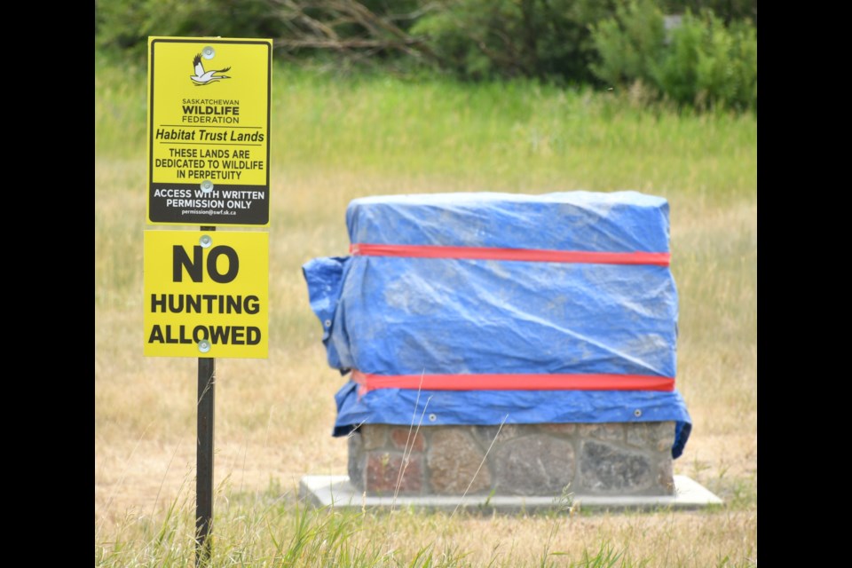 A Saskatchewan Wildlife Federation sign indicates that the nearby grasslands are protected, while a dedication monument waits to be uncovered. Photo by Jason G. Antonio