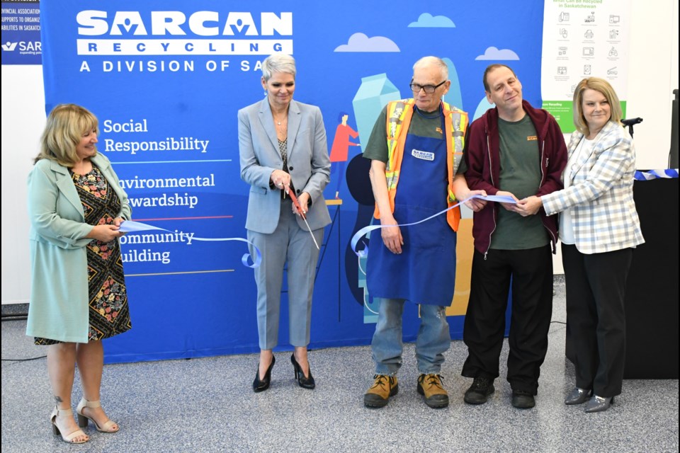 Christine Tell (second from left with large scissors) cuts the ribbon to formally announce the opening of SARCAN's new facility at 52 Highland Road.