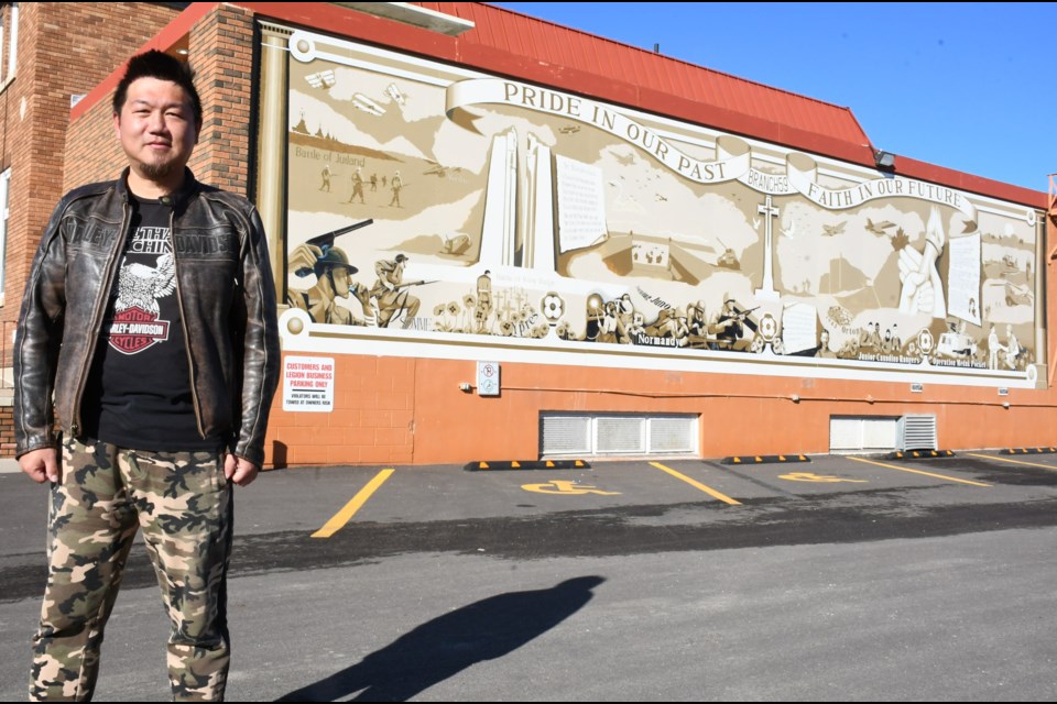 Xinzheng Liu poses near the mural that he updated and enhanced on the side of the Royal Canadian Legion building. Photo by Jason G. Antonio  