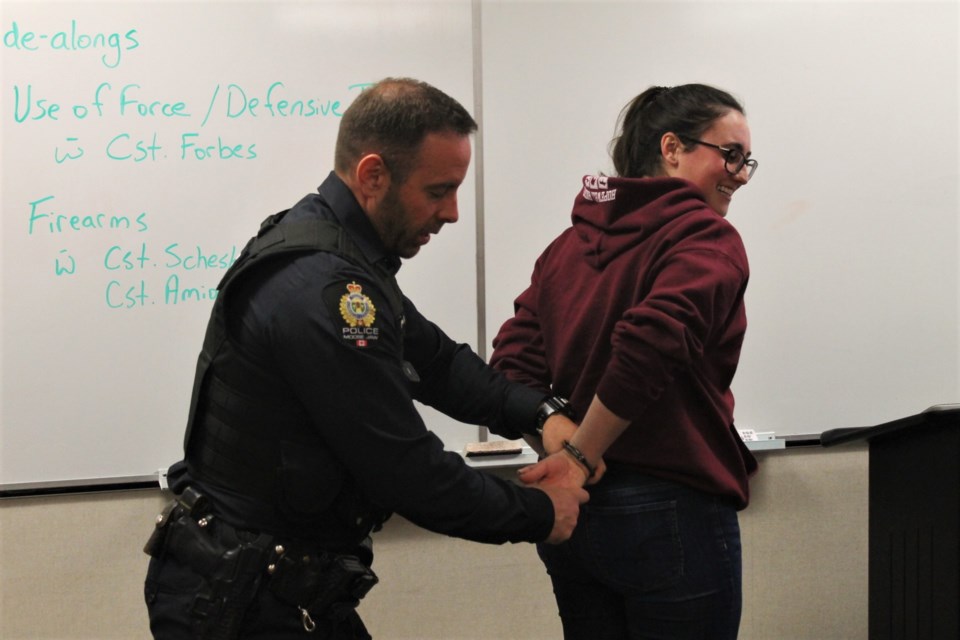 Const. Ryan Forbes demonstrates the very particular way that officers handcuff an individual, with Community Police Academy attendee Jessie playing the perp. 