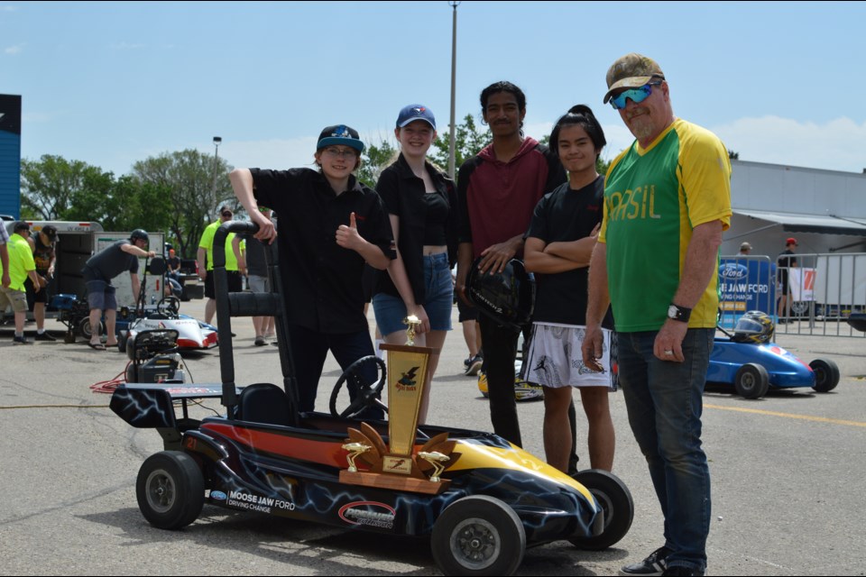 Rowan, Haylee, Wayne, and Darryl, members of the Vanier Velocity team, pose with Merv Armstrong, their EV kart, and the student challenge trophy.