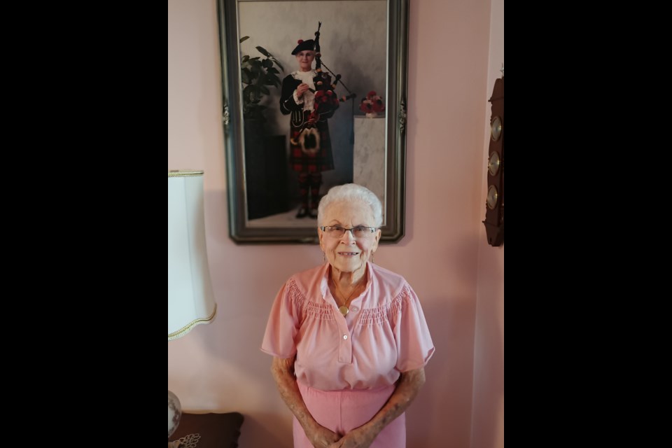 Marie Victoria Gibbs stands before her picture with her Clan Wallace kilt on her 100th birthday.