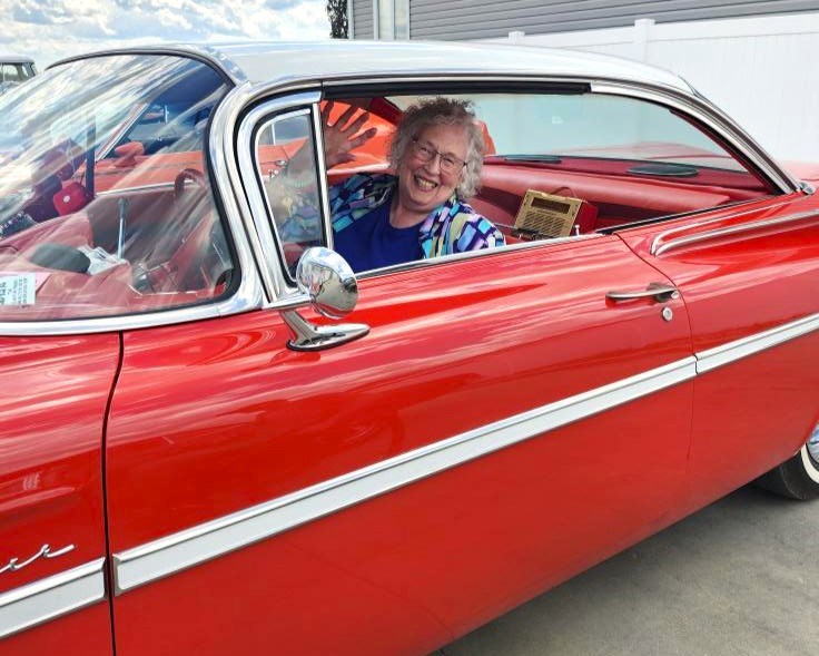 Points West resident Carolyn smiles from the driver’s seat of a red vintage car during the community’s on-site classic car show.