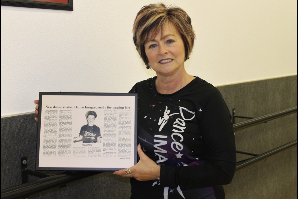 Owner Barb Jackman stands with the framed article detailing the opening of Dance Images by BJ 30 years ago.