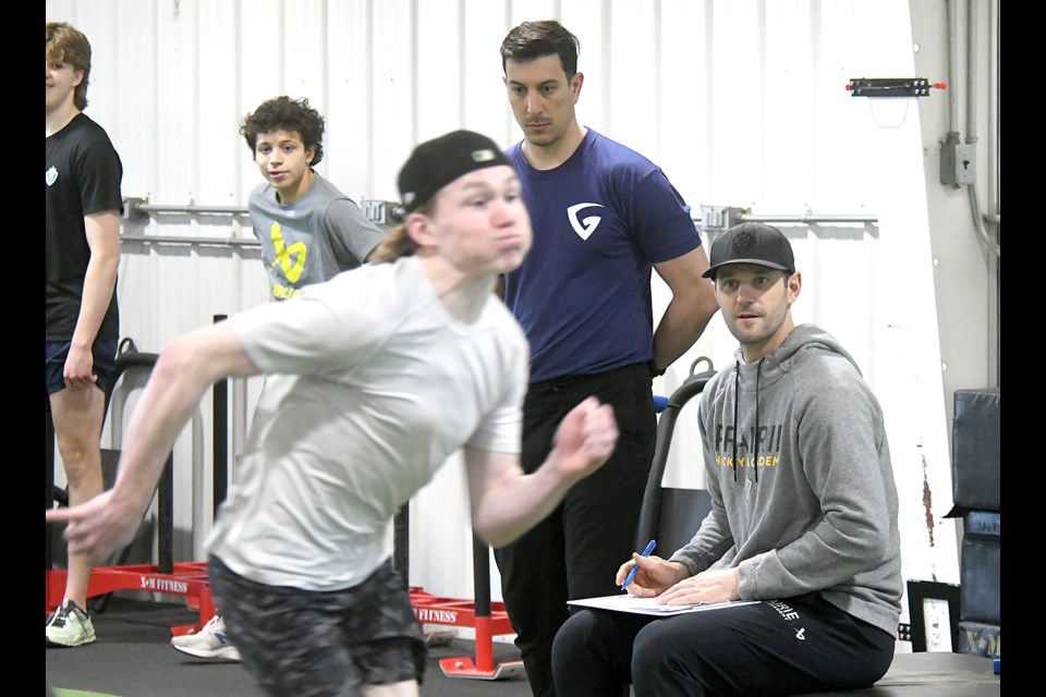 Gary Roberts High Performance Training strength and conditioning coach Lucas Azeredo Lobo and Prairie Hockey Academy director of performance Dustin Friesen (seated) look on as camp participants run sprints.