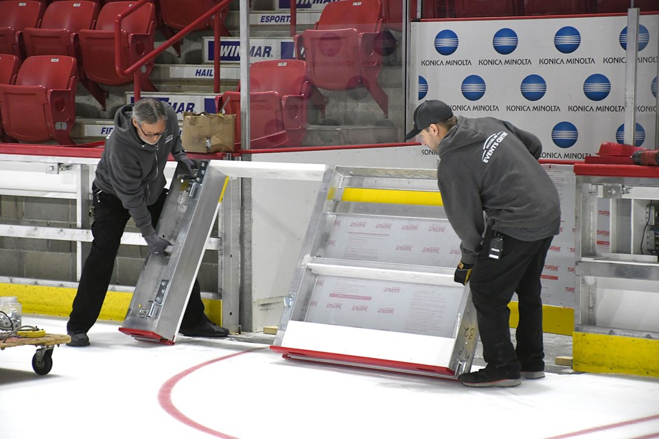 Moose Jaw Events Centre workers lift a section of boards into place at the timekeepers bench.
