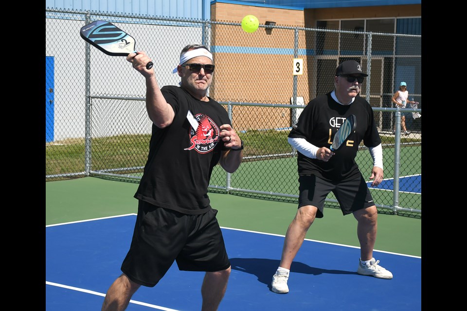 Moose Jaw city councillor Jamey Logan hits a return as Mayor Clive Tolley keeps an eye on their opponents during a special exhibition match after the grand opening.