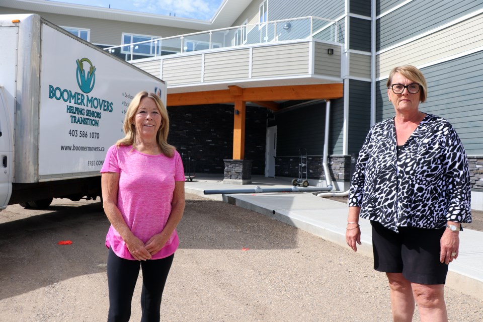Connie Huelsman (right) and Barb Lewis outside the entrance of the new Autumn Grove residential facility as movers arrive with seniors' belongings.  Johnnie Bachusky/MVP Staff