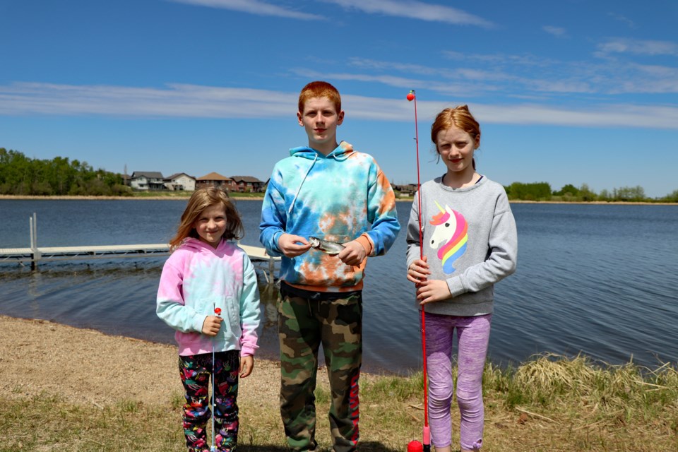 Thirteen-year-old Cian Kelly (centre) holds a caught rainbow trout on May 22 at Dodd's Lake, which was stocked with 330 of the popular sport fish earlier in the day by the Innisfail Lions Club. Cian's angling efforts were joined by six-year-old sister Leah (left) and older sister Michaela, 13. The children and their parents, who came to Canada eight years ago from Ireland, are residents of Cochrane. Johnnie Bachusky/MVP Staff 