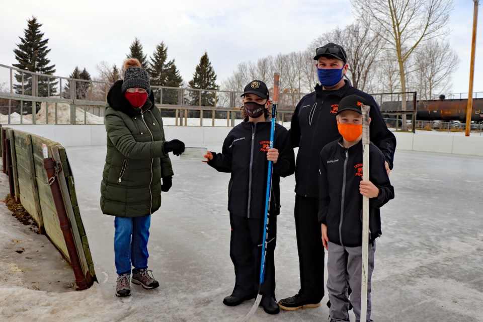 Judy Cooper, co-coordinator of the Innisfail and District Food Bank, left, receives a $500 cheque from Innisfail's U13 Palliser Chevrolet Flyers team on March 6 at the outdoor rink at 54th Avenue and 37th Street. Joining her is team head coach Kelly Mayhew, his son Elliot and Konner Attwell. Johnnie Bachusky/MVP Staff.