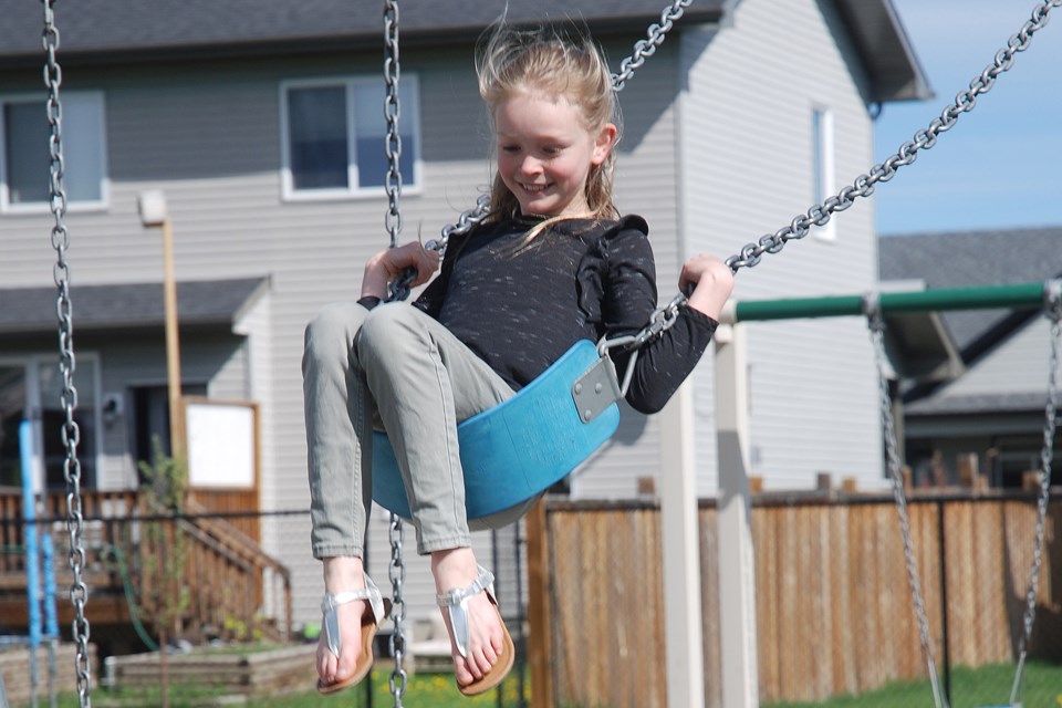 SMILE SAYS IT ALL — Less than one hour after the playground in Sundre's northeast subdivision along 11A Avenue was reopened on Monday morning, Sadie Winters, 9, enthusiastically came out to play on the swings with her sister Georgia, 11, and their cousin Reuben Baber, 12, who was visiting from Balzac. 