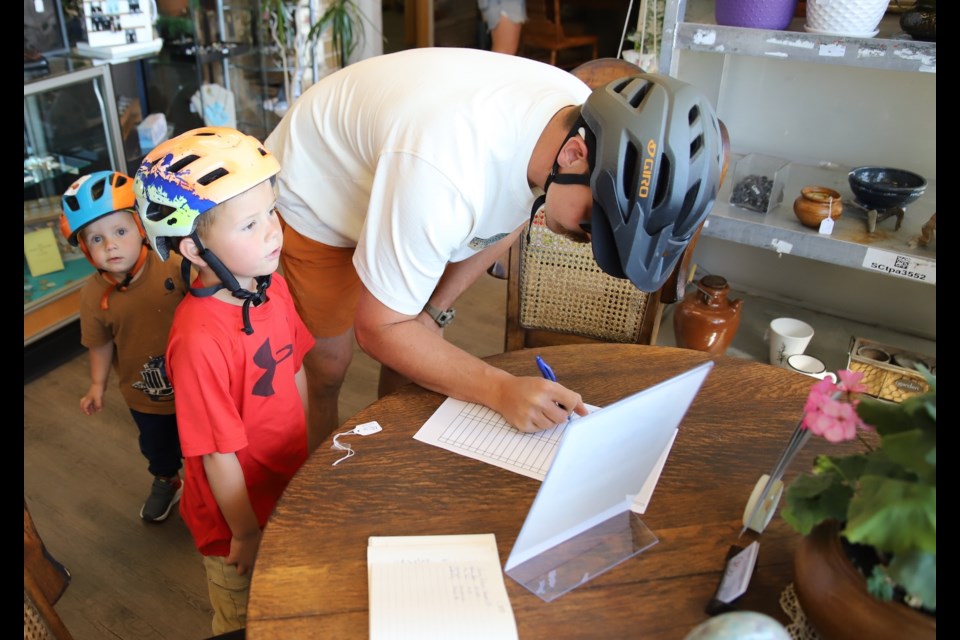 Michael Stone signs a sheet to show that the family, including Ezra, 5,  Cooper, 2 and their mom Charilyn, found Triple R Consignment, one of the participating businesses in the second annual Bike For History scavenger hunt, held Saturday in Uptowne Olds.
Doug Collie/MVP Staff