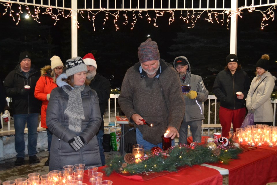 Dennis McKernan lights candles in the Olds Centennial Park gazebo to represent various aspects of bereavement as his wife Nan and other Tree of Remembrance participants look on. 