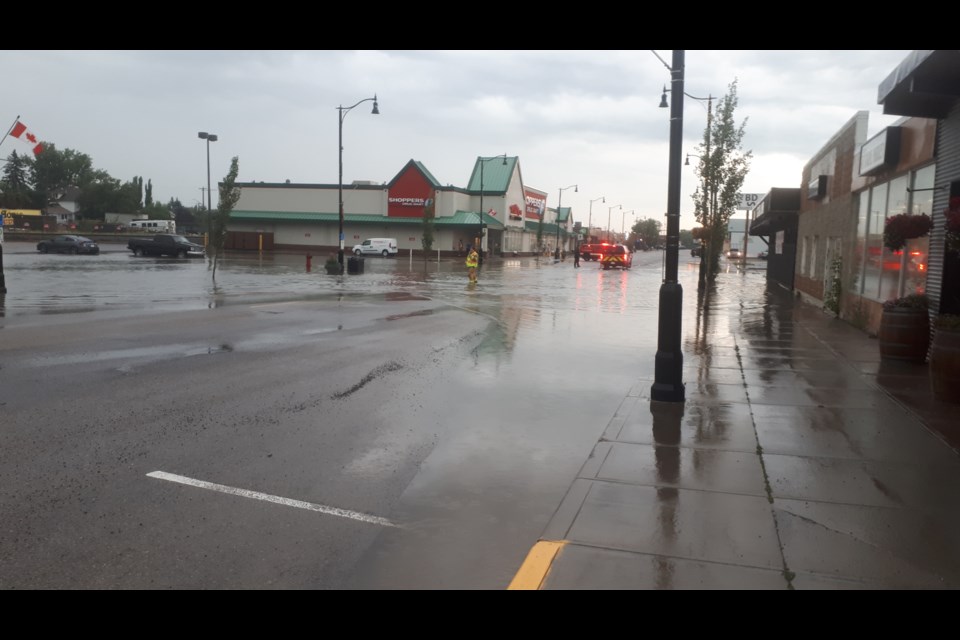 A firefighter watches as water floods onto 50th Avenue from the parking lot next to the Wildrose Medical Centre.