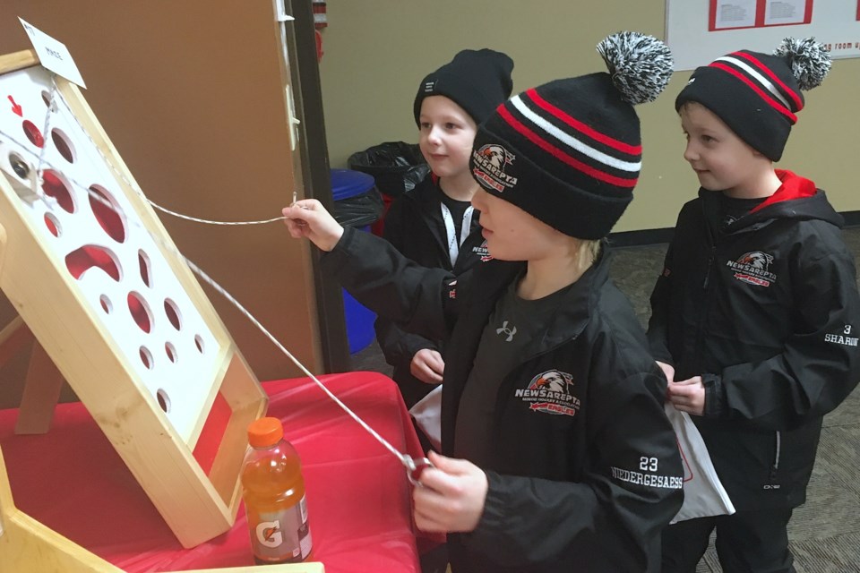 PULLING STRINGS – Samuel Niedergesaess, from a community southeast of Edmonton called New Sarepta, pulls some strings on Saturday afternoon as he carefully attempts to navigate a little metal ball through a perilous maze of trap doors to the main prize highlighted by a red arrow while his friends Beau Sharun, left, and Jake Sharun look on. The game was among several side activities including a silent auction fundraiser being hosted in the Sundre Arena’s lounge area while the Huskies U9s home tournament played on.
Simon Ducatel/MVP Staff