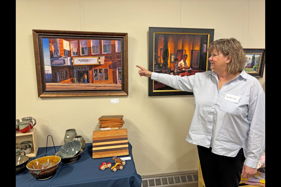 Jacalyn Carr, co-organizer of Innisfail's second Artisan Exhibition & Sale, points out the paintings of professional local artist Michael Downs during the event on April 26. Johnnie Bachusky/MVP Staff