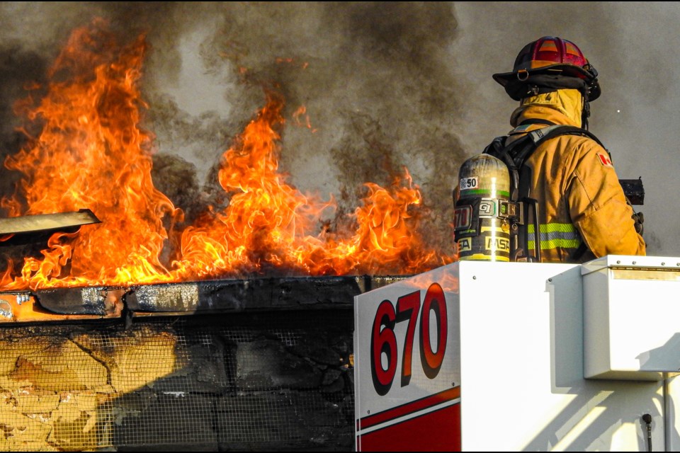 The roof of a two-story historical Globe Coliseum building in downtown Innisfail is ablaze during the early morning hours of Aug. 2 as a firefighter perched high on an aerial platform prepares to battle the intense flames. Photo by David M. Nagy