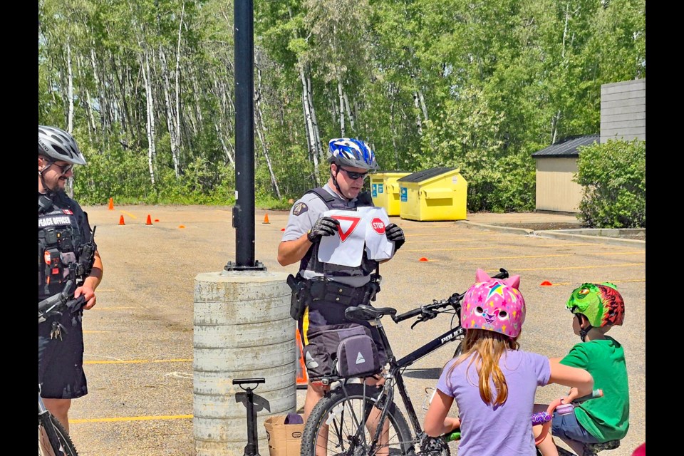 Innisfail RCMP Const. Craig Nelson (right-standing) and Senior Peace Officer Sgt. Derek Radatzke show kids street sign symbols during a break on the obstacle course at the 5th annual Innisfail RCMP Bike Rodeo on May 24. Submitted RCMP photo