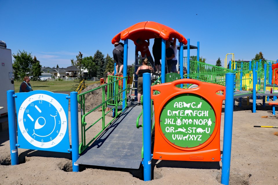 A completed entrance gate into Innisfail's all-inclusive playground with volunteers at work in the background on another facility feature. Johnnie Bachusky/MVP Staff