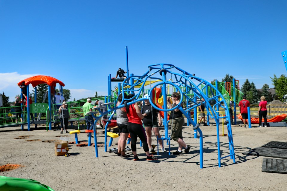 Volunteers gather under a nearly completed playground feature. On Aug. 12, there was more than 25 volunteers at the site, with many coming from out of town to help. Johnnie Bachusky/MVP Staff